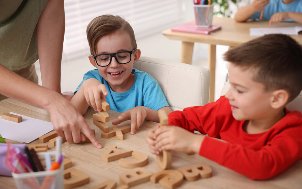 Little boys having lesson with teacher at wooden desk