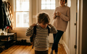 young child getting ready for school in the morning at home, putting on a backpack
